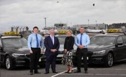 Christopher McCausland and Katy Best stand in front of two Value Cabs cars along with two drivers.